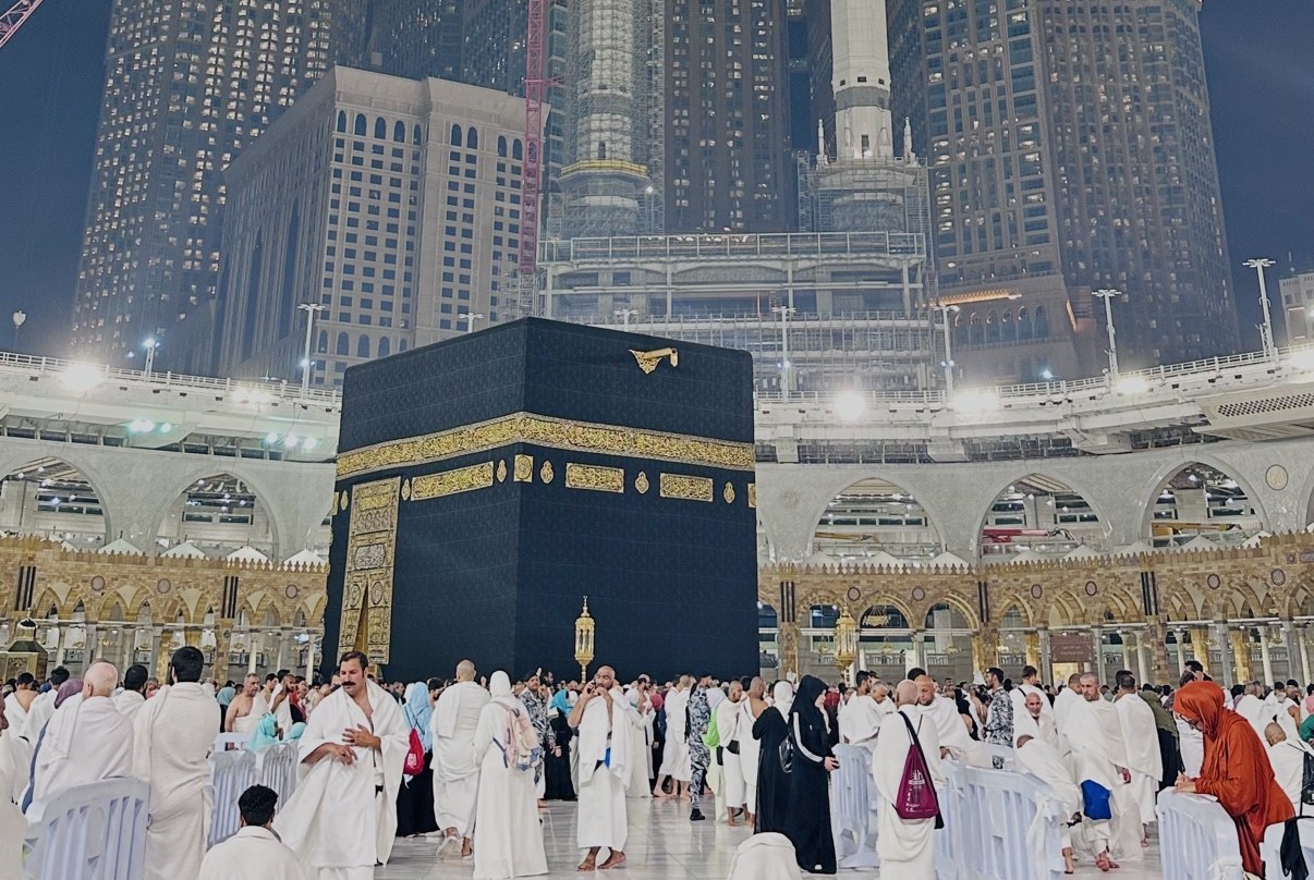 The Kaaba at night in Makkah, pilgrims gathered around it beneath the illuminated clock tower