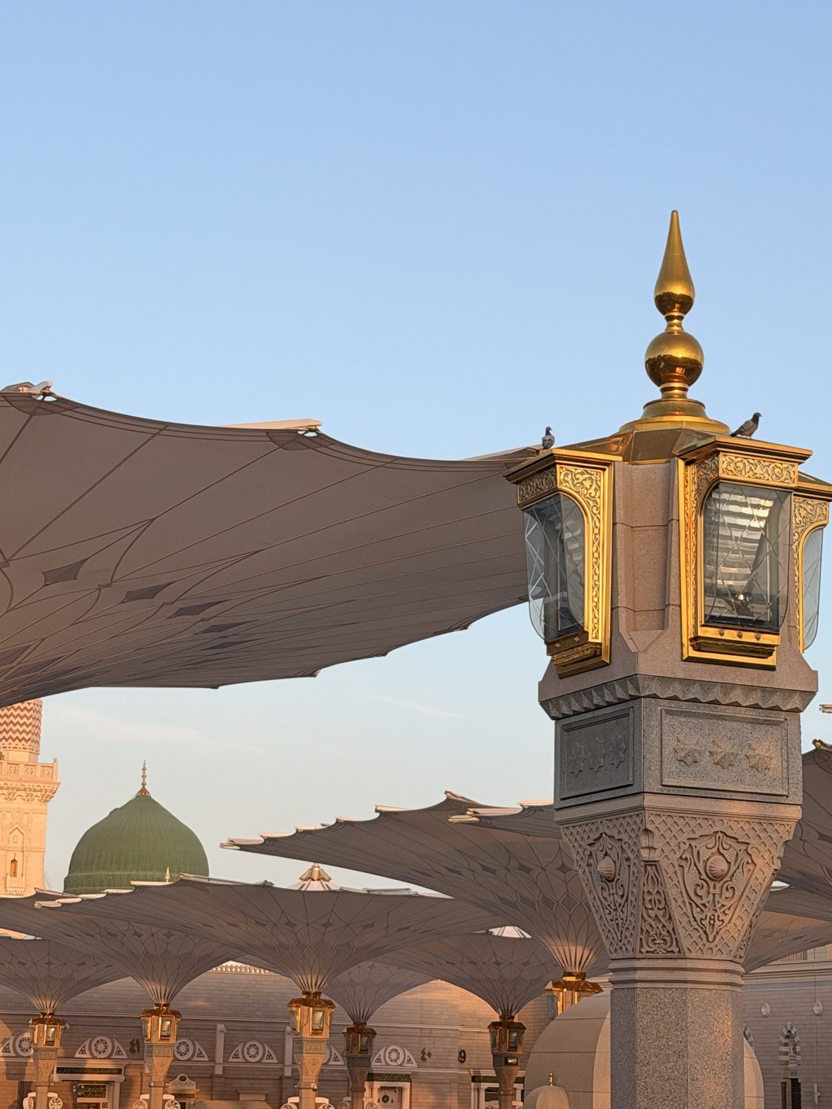 Golden detail atop a minaret of the Prophet's Mosque, courtyard umbrellas below