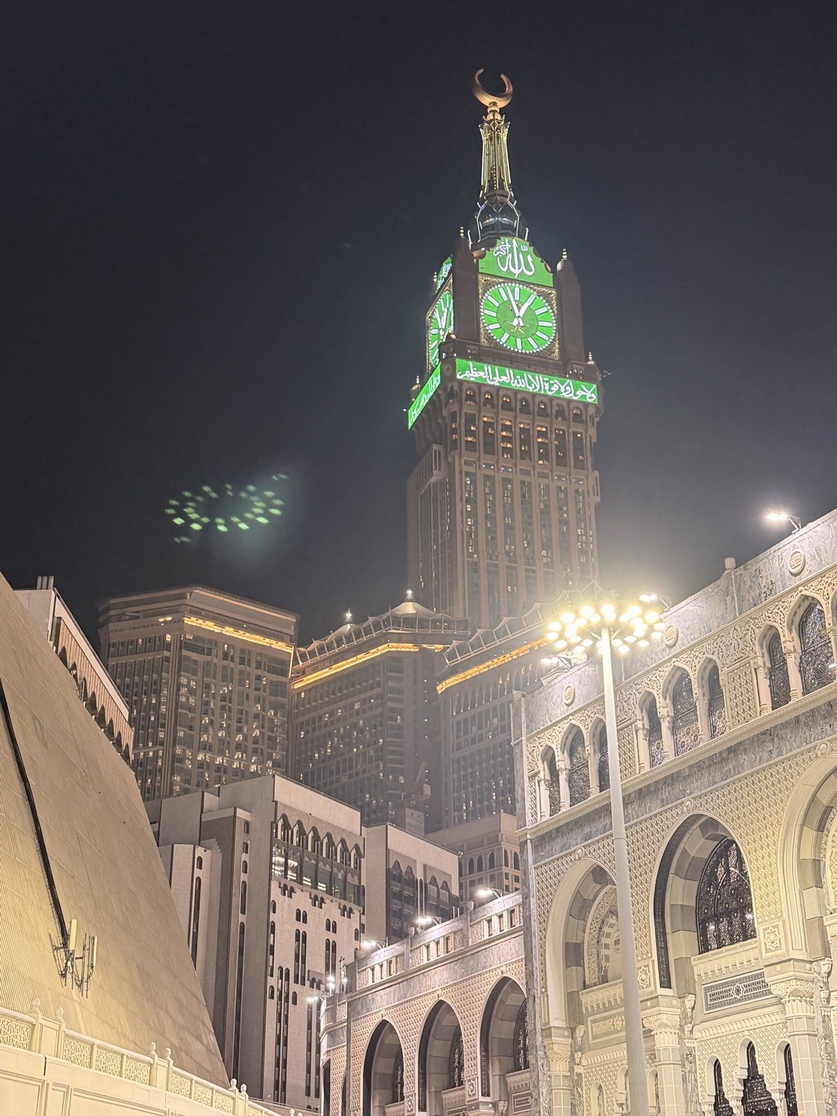 The Makkah clock tower glowing green above the Grand Mosque at night