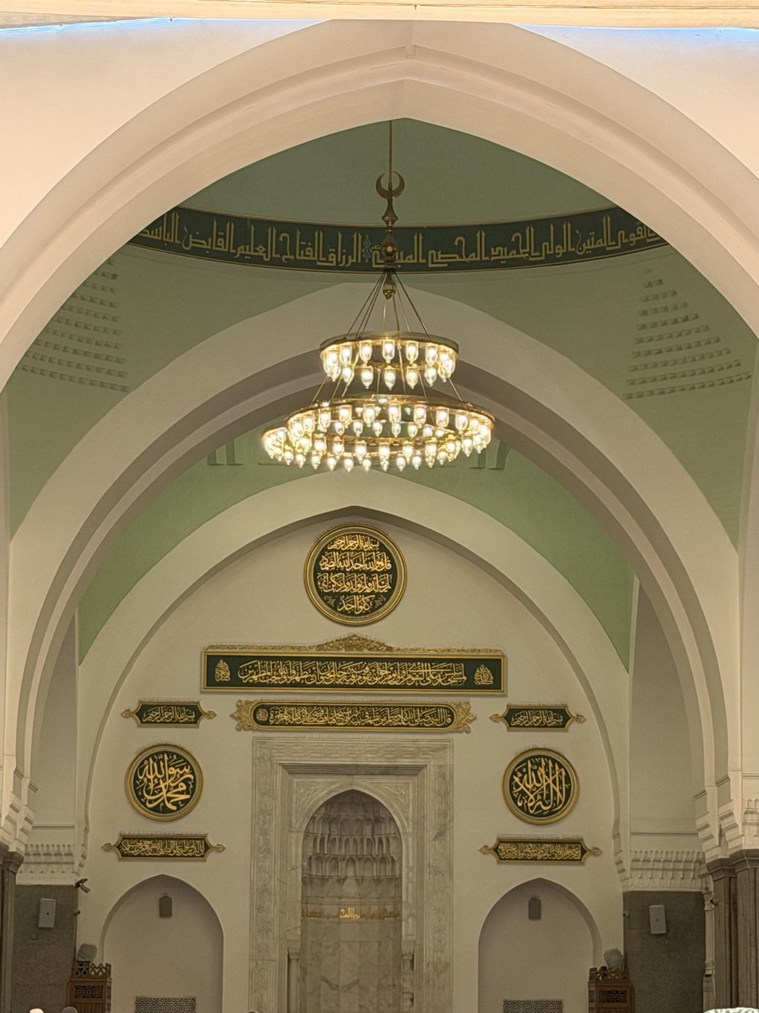 The mihrab and calligraphy inside Masjid Quba beneath a hanging chandelier
