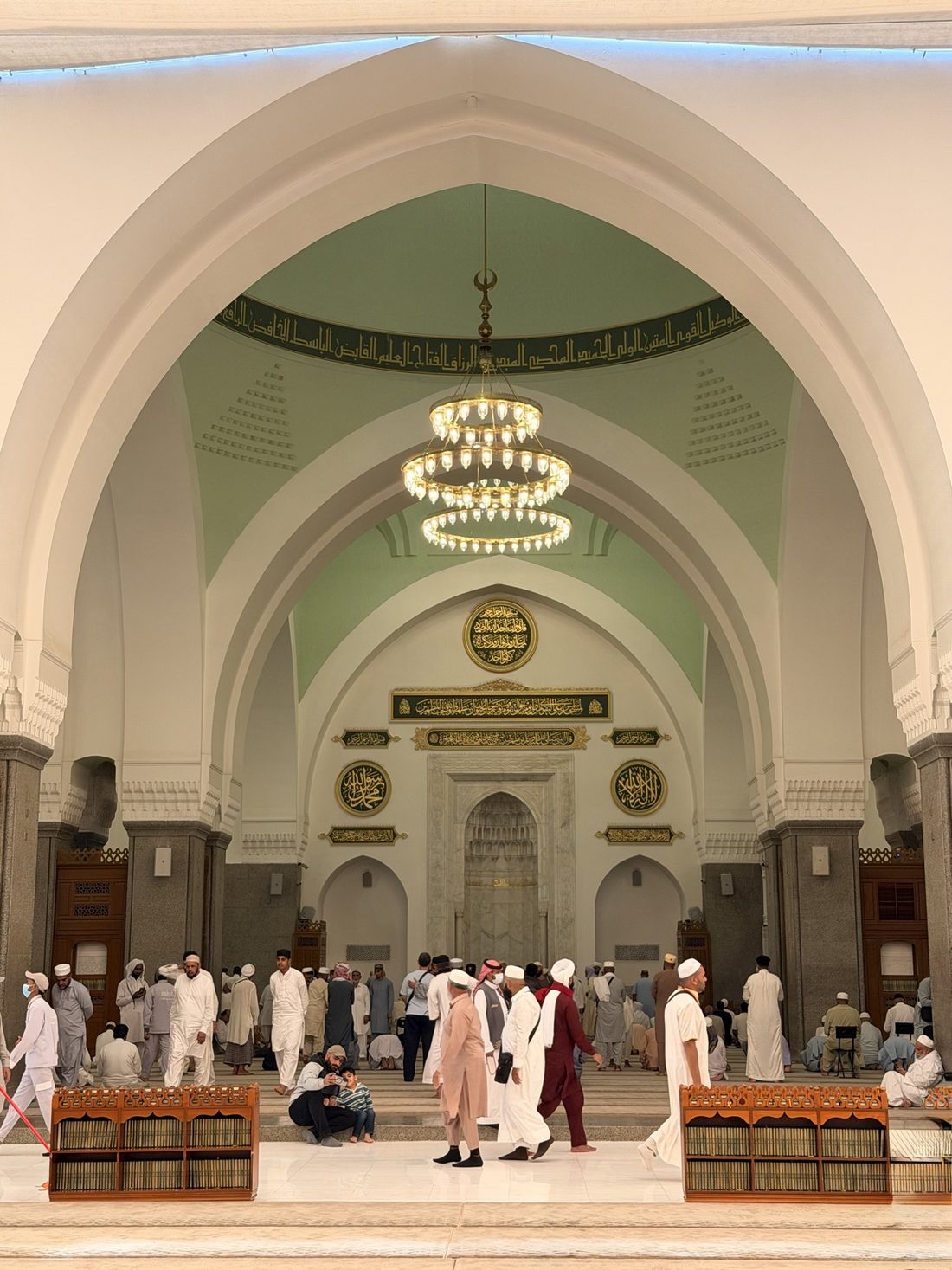 Worshippers inside Masjid Quba before its mihrab and chandeliers