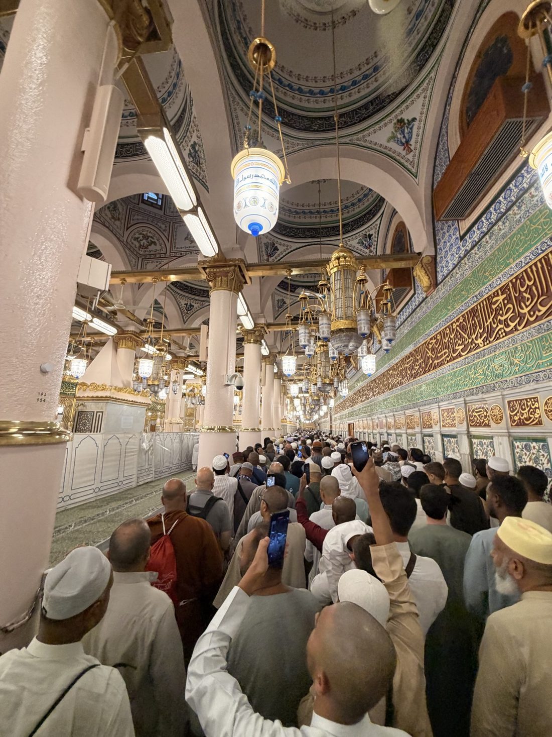 Pilgrims moving through the Rawdah corridor beside the Prophet's chamber, phones raised