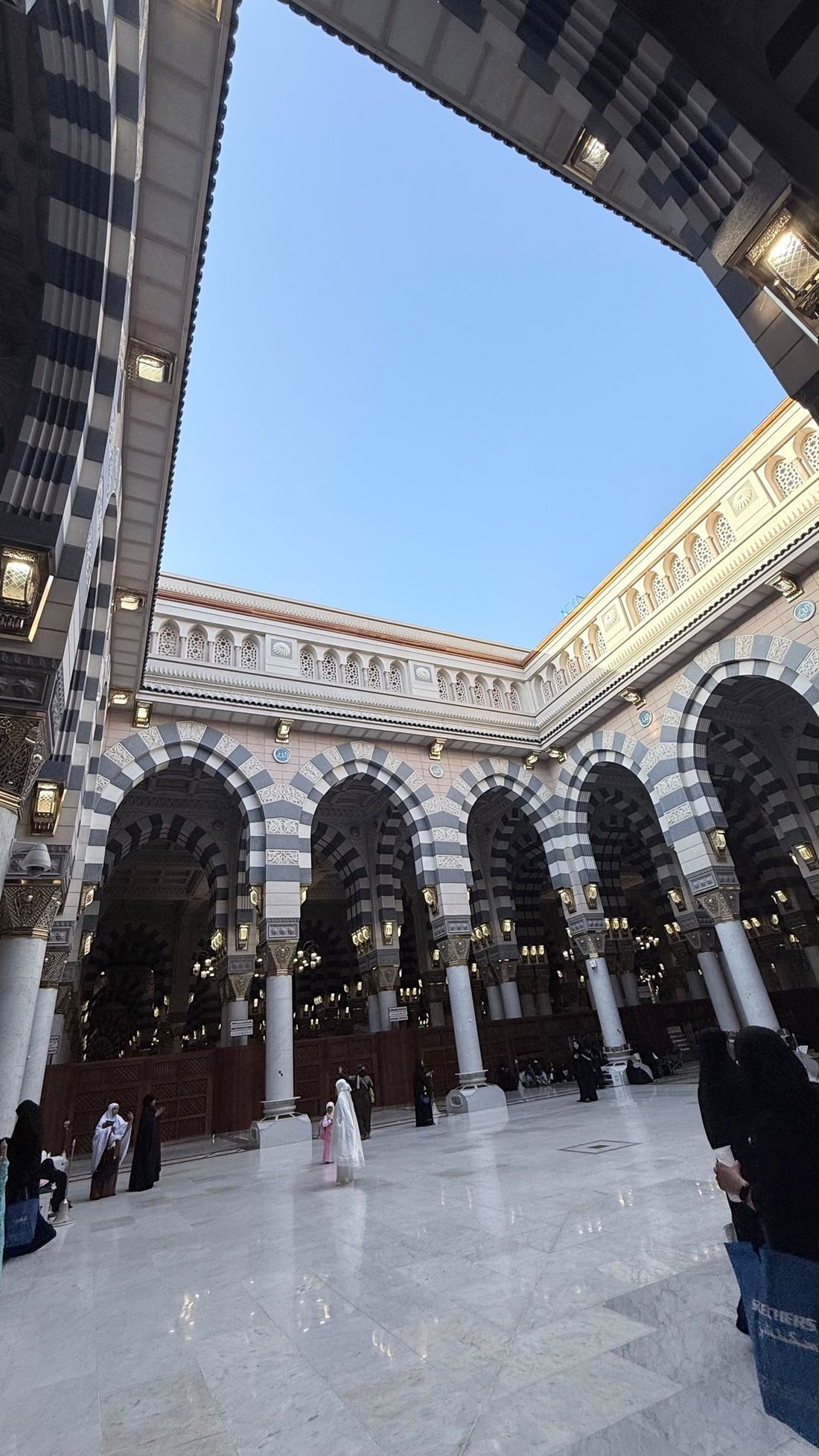 An open-air courtyard inside the Prophet's Mosque, striped arches under a blue sky